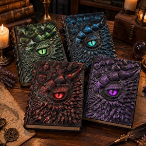 Puede incluir: Cuatro diarios rectangulares con cubiertas texturizadas que presentan escamas de dragón en relieve, un cuerno prominente y un ojo central. Los diarios son de color verde, azul, rojo y morado, cada uno con un color de ojo a juego y escamas.