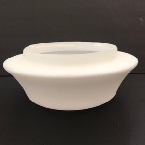 May include: A white, opaque glass lampshade with a flared, bowl-like shape. The shade has a rounded base and a cylindrical top, designed to fit over a light fixture. The overall design is simple and functional.
