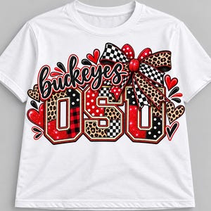 May include: A white short-sleeved t-shirt featuring a graphic design with the word Buckeyes in black script above the letters OSU. The design includes a large bow, red hearts, and patterns of leopard print, red plaid, and black and white polka dots.