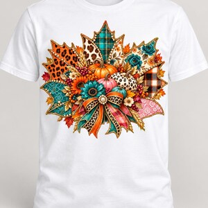 May include: A white t-shirt featuring a large, central graphic of a maple leaf shape composed of various patterns including leopard print, plaid, and floral designs. The graphic includes pumpkins, sunflowers, and a decorative bow with a pearl center.