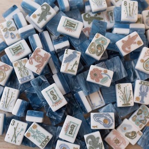May include: A collection of rectangular mahjong tiles featuring a white face with engraved illustrations of lobsters, crabs, herons, oysters, and bamboo stalks, paired with a marbled blue and white back. Each tile displays unique symbols and numbers.