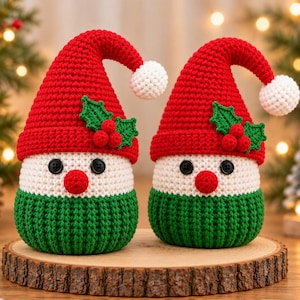 Pode incluir: Dois gnomos de crochê feitos à mão com gorros vermelhos pontiagudos, pompons brancos, folhas de azevinho verdes e bagas vermelhas. Cada gnomo tem um rosto branco com olhos de botão pretos, um nariz redondo vermelho e uma base verde canelada.