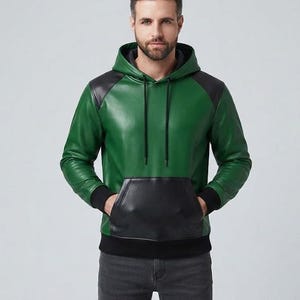 Puede incluir: Una sudadera con capucha de cuero verde que presenta paneles de cuero negro en los hombros, un bolsillo canguro delantero de cuero negro, puños y dobladillo acanalados en negro, y cordones negros. Se lleva con pantalones vaqueros gris oscuro.