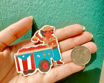 May include: A die-cut sticker featuring a person with a moustache and tan cap ringing a bell while standing behind a blue cart. The cart displays the Puerto Rican flag and text, and is positioned next to a coin for scale.