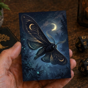 May include: A rectangular card featuring a dark, detailed illustration of a moth with golden crescent moon patterns on its wings. The moth is set against a night sky with a glowing crescent moon, silhouetted trees, and small, bright light specks.