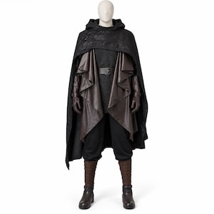 May include: A costume set featuring a black hooded cloak with buckle detail, a dark brown open-front vest, a dark grey tunic with a belt, black trousers, brown arm wraps, and dark brown boots displayed on a mannequin against a white background.