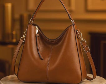 May include: A medium-sized brown hobo bag featuring a single top handle, a detachable shoulder strap with gold-toned metal hardware, a central vertical seam, and a top zipper closure with a long leather pull tab for easy access to the main compartment.