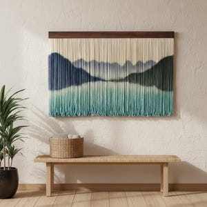May include: A rectangular wall hanging featuring a dark wood top bar with numerous vertical cream-coloured strings. The strings are dyed in a gradient pattern, transitioning from deep navy blue at the top to a soft teal green at the bottom.