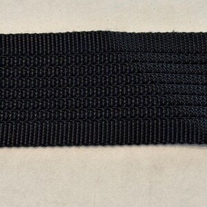 May include: Black woven webbing strap. The strap is made of a durable material and has a smooth, even texture.