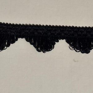 May include: Black fringe trim with a scalloped edge. The trim is made of a woven material and has a decorative, textured appearance. This trim is suitable for various sewing and craft projects.