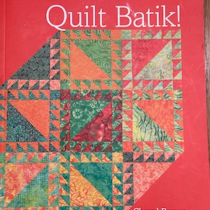 Op de afbeelding: Een boek getiteld "Quilt Batik!" van Cheryl Brown, met een kleurrijk patchwork-ontwerp op de omslag. Het boek is rood met een witte titel en auteursnaam.