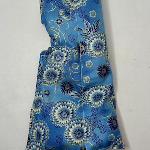 May include: A blue and white floral patterned fabric eye pillow with gold accents. The pillow is filled with rice and lavender.