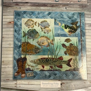 Peut inclure: Une courtepointe complète intitulée "Something Fishy" représentant divers poissons, tortues et plantes aquatiques. La courtepointe mesure 112 x 107 cm et comprend le texte "Something Fishy" en haut et en bas. La courtepointe a un code couleur bleu et vert.