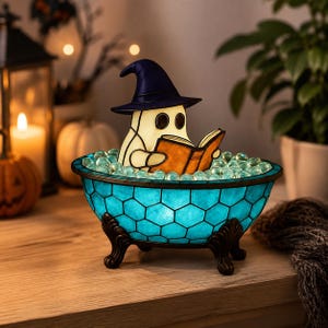 May include: A stained glass lamp shaped like a bathtub with a blue honeycomb pattern and dark metal claw feet. Inside the tub, a cream-colored ghost figure wearing a dark purple pointed hat sits and reads an open orange book amidst clear glass bubbles.