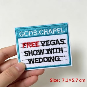 May include: A rectangular embroidered patch measuring 7.1 by 5.7 cm with a teal border. The top section features the white text GCDS-CHAPEL. The white lower section contains the black text FREE VEGAS SHOW WITH WEDDING, with FREE in red.
