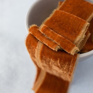 Könnte beinhalten: Eine Schüssel gefüllt mit einem Stapel verbrannt-orangenfarbener Samtband mit ausgefransten Kanten.