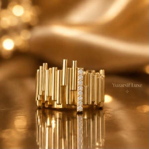May include: A gold ring featuring a series of vertical, varying-length bars arranged in a row. One prominent vertical bar is set with a line of small, clear, round-cut stones. The text Yuzarsif Luxe is visible to the right of the ring.