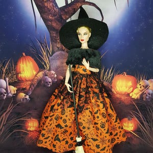 Puede incluir: Una muñeca de bruja con un sombrero de bruja negro, una estola de piel negra y un vestido naranja y negro con estampado de Halloween. La muñeca sostiene una escoba y está de pie frente a un telón de fondo de temática de Halloween con calabazas y calaveras.