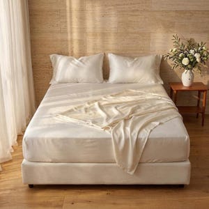 May include: A bed featuring a white fitted sheet, two matching white pillowcases, and a draped white throw blanket. The bedding set is arranged on a mattress with a white base, creating a clean and neutral aesthetic for a bedroom sleeping space.