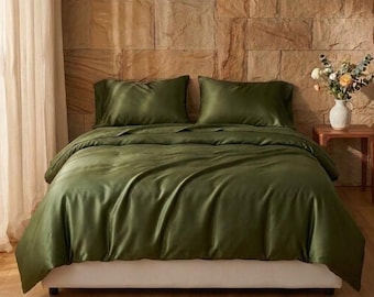 Puede incluir: Una cama con una funda nórdica de color verde oliva sólido y dos fundas de almohada a juego. La ropa de cama tiene un acabado suave y brillante, y está colocada sobre una base de colchón blanca. El conjunto ofrece un color uniforme.