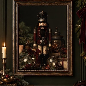 Op de afbeelding: Een ingelijste kunstdruk met een notenkraker in vintage-stijl in een donkerrood en zwart uniform, omringd door dennentakken, glazen ornamenten, dennenappels en ingepakte cadeaus in een sfeervolle, donkere kerstsetting.