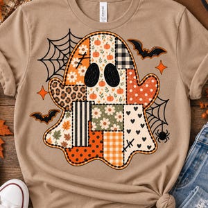 May include: A tan t-shirt featuring a large ghost graphic composed of various patchwork patterns including pumpkins, flowers, leopard print, stripes, polka dots, and hearts. The design is accented with black spiderwebs, bats, and stars.
