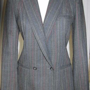 May include: A gray blazer with thin red and blue stripes. The blazer has a double-breasted closure with two buttons and a flap pocket on the left side.