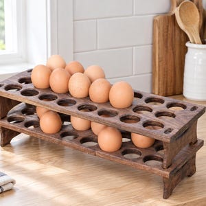 May include: A two-tiered dark brown wooden egg holder with a rectangular frame and multiple circular cutouts. Several light brown chicken eggs are nestled within the top and bottom rows of the stand, which features a sturdy base and open design.