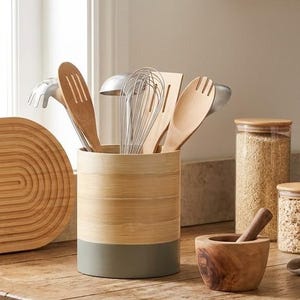May include: A cylindrical bamboo utensil holder with a solid gray base, filled with various wooden and metal kitchen tools including a whisk, spatula, and spoons. The holder features a natural light wood grain finish on the upper portion.