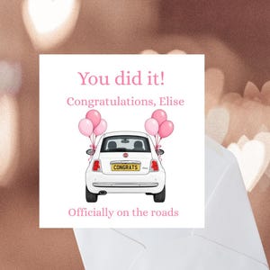 Peut inclure: Une carte de vœux carrée illustrant une voiture blanche vue de l'arrière, décorée de ballons roses de chaque côté. Le texte indique : You did it! Congratulations, Elise. Officially on the roads. La plaque d'immatriculation affiche CONGRATS.