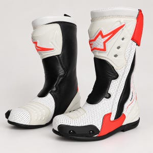 Puede incluir: Un par de botas de moto Alpinestars en blanco, negro y rojo brillante. Las botas cuentan con paneles de cuero blanco perforado, secciones negras sólidas y elementos protectores moldeados en la espinilla, el tobillo y la puntera con detalles en rojo.