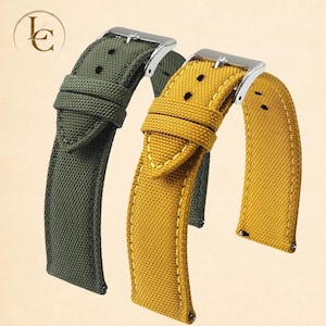 May include: Two watch straps made of a textured fabric material, one in olive green and one in mustard yellow. Each strap features a silver-toned metal buckle, a matching fabric keeper loop, and visible stitching along the edges with pin holes.