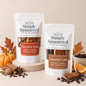 May include: Two white stand-up pouches labeled Simply Simmered. The left pouch contains a Pumpkin Spice simmer pot blend with visible dried orange, cinnamon, and spices. The right pouch contains a Cinnamon Latte blend with coffee beans and orange slices.