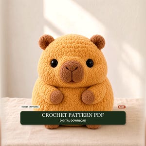 Peut inclure: Une peluche capybara crochetée jaune doré avec des oreilles, un nez et des pattes marron foncé, dotée de grands yeux noirs. Une étiquette rectangulaire vert foncé affiche le texte blanc : HONEY CAPYBARA, EASY, CROCHET PATTERN PDF, DIGITAL DOWNLOAD.