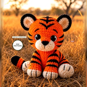 Può includere: Un peluche a forma di tigre realizzato all'uncinetto con filato arancione brillante, strisce nere e muso e zampe color crema. Il giocattolo presenta grandi occhi neri di sicurezza e un piccolo naso nero. Il testo recita: INSTANT DOWNLOAD, PDF PATTERN, EASY.