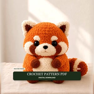 Könnte beinhalten: Ein Plüsch-Panda aus rostorangefarbenem und cremefarbenem Garn mit großen schwarzen Augen und einer kleinen schwarzen Nase. Ein dunkelgrünes rechteckiges Etikett vorne zeigt den Text: RUST RED PANDA, CROCHET PATTERN PDF, EASY, DIGITAL DOWNLOAD.
