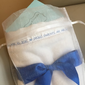 May include: A white cloth bag with a blue ribbon bow. The bag has the text "Proud Parents are Mike and" embroidered on it.