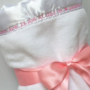 May include: White baby blanket with a pink satin ribbon tied in a bow. The blanket has a white satin border with pink embroidery that reads "June 23, 2016 at 12:52 PM".