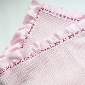 May include: A pink waffle weave baby blanket with a satin trim and embroidered hearts and flowers. The blanket is personalized with the text "OVAN BORN ON SEPTEMBER 6, 2016 AT 303 PM".