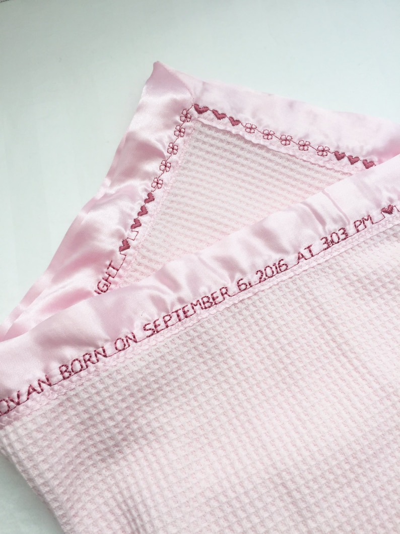 May include: A pink waffle weave baby blanket with a satin trim and embroidered hearts and flowers. The blanket is personalized with the text "OVAN BORN ON SEPTEMBER 6, 2016 AT 303 PM".