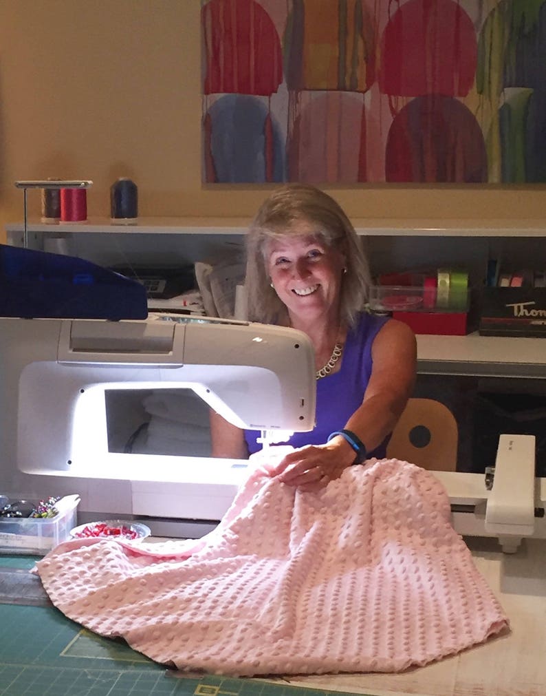 May include: A woman is using a sewing machine to sew a pink quilted fabric. The fabric is on a green cutting mat. The sewing machine has a bright light shining on the fabric.