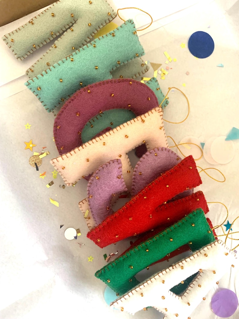 May include: A set of felt letters with gold bead accents, spelling out the word "MADE". The letters are in various colors, including green, pink, purple, red, and white.