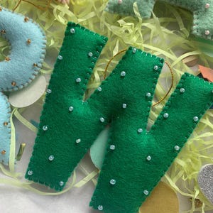 May include: Green felt letter W with white beads sewn on. The letter is handmade and has a gold string attached.