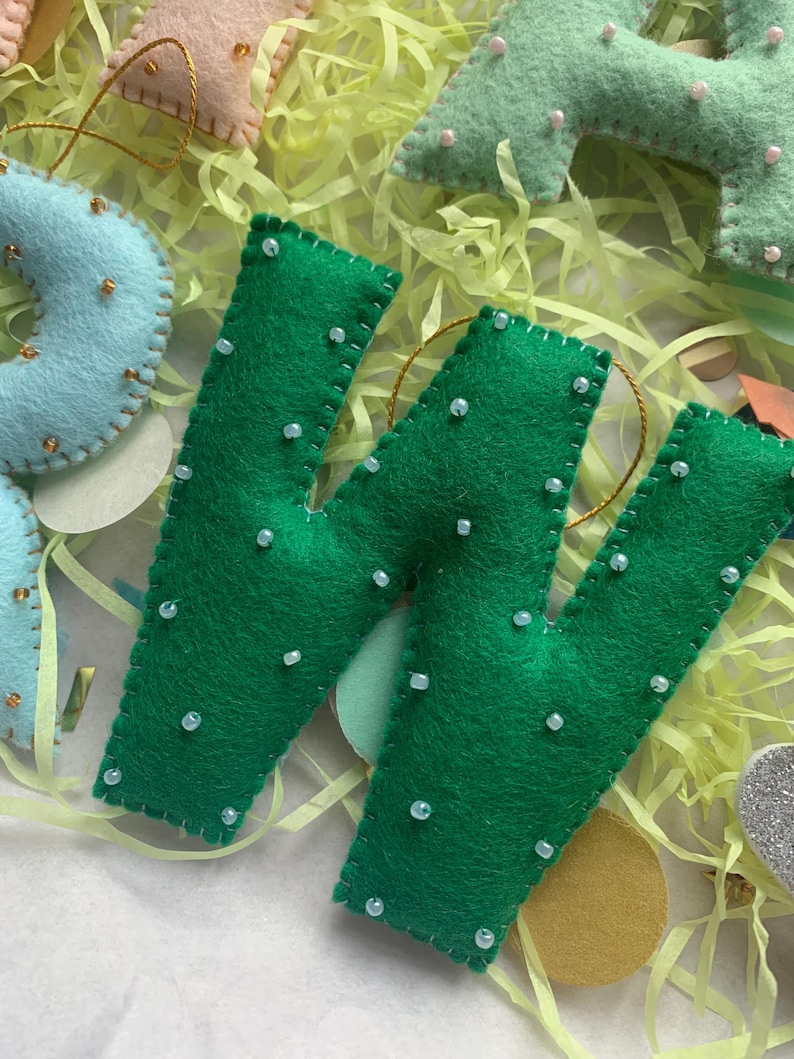 May include: Green felt letter W with white beads sewn on. The letter is handmade and has a gold string attached.