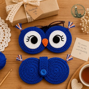 May include: A blue crochet owl-shaped glasses case featuring large white eyes with black pupils and long eyelashes, an orange beak, and small tufts of orange, white, and blue yarn at the corners. The case includes a blue button closure.