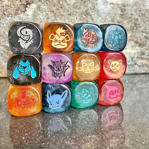 Pode incluir: Um conjunto de doze dados translúcidos e multicoloridos dispostos em uma grade. Cada dado apresenta um ícone de personagem gravado único em sua face, incluindo vários designs de criaturas em cores como preto, laranja, azul, roxo, amarelo, vermelho e verde.