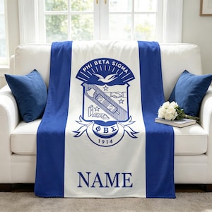 Peut inclure: Un plaid bleu et blanc arborant l'emblème de la fraternité Phi Beta Sigma au centre, incluant une colombe, des mains jointes et le texte Phi Beta Sigma 1914. Le mot NAME est imprimé en grandes lettres capitales bleues en bas.