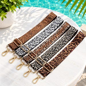 Pode incluir: Cinco alças ajustáveis para bolsas com vários padrões de leopardo em tons de castanho, preto, branco e cinzento. Cada alça possui ferragens metálicas douradas, incluindo fivelas deslizantes para ajuste de comprimento e mosquetões giratórios.