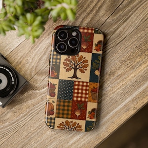 May include: A smartphone case featuring a patchwork design of autumn-themed squares. The pattern includes illustrations of a central tree, pumpkins, baskets of apples, radishes, and oak leaves, combined with plaid, gingham, and polka dot fabric textures.