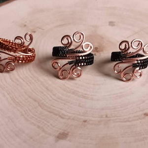 May include: Three wire-wrapped rings featuring intricate coiled designs. The ring on the left is made of copper-coloured wire, while the two rings on the right feature a combination of black wire and copper-coloured wire accents in a spiral pattern.